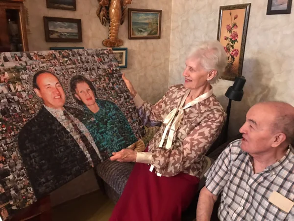 Юбилярша держит картину из фотографий, рядом сидит юбиляр: вручение подарка от детей